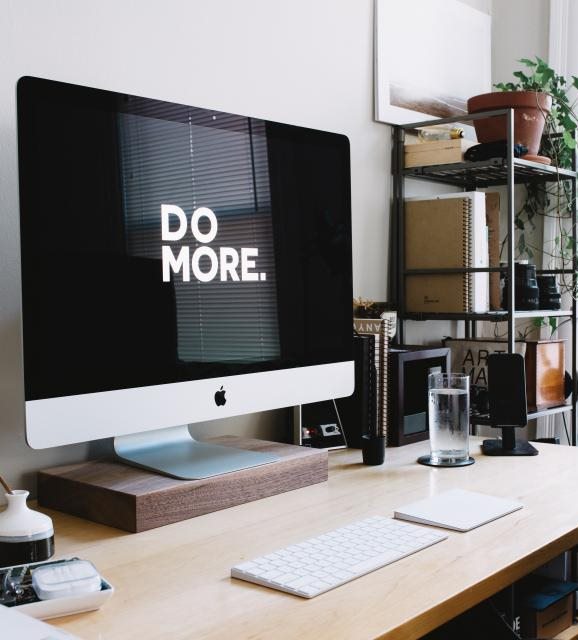 A modern office desk with an iMac showing the words Do More