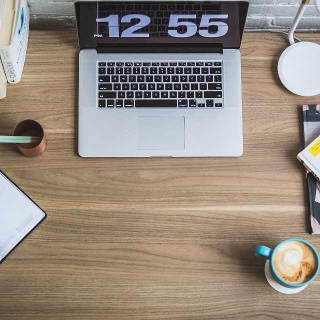 A tidy work desk seen from above with a laptop and a clock